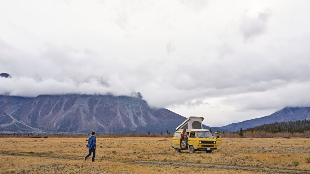 A couple in a wide field in Saskatchewan with mountains behind them